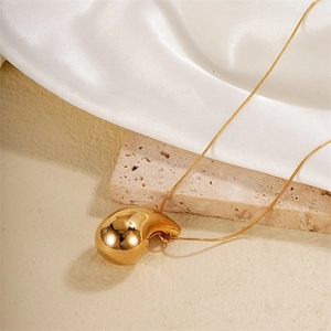 Detail of high-polished gold teardrop pendant on a sleek snake chain over silk and stone