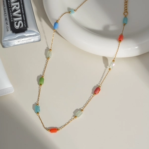 Detail of a gold chain necklace with colorful beads on a white ceramic plate