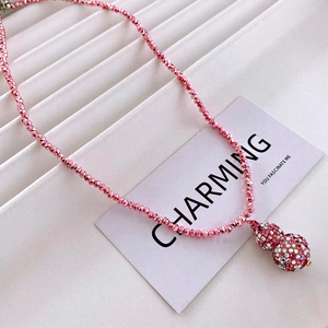 Macro detail of a pink beaded necklace with a crystal-encrusted gourd pendant on fabric