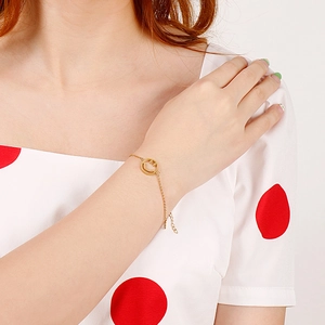 Detail of gold smiley face pendant on a delicate chain bracelet worn on a model's wrist