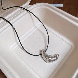 Silver croissant pendant necklace on black cord displayed in a creative food box case