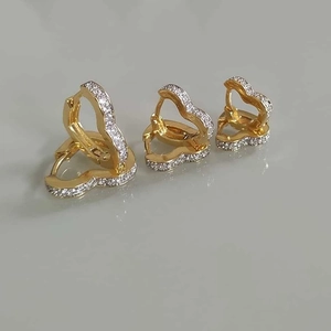 Detailed view of three pairs of golden heart hoop earrings with sparkling zircon stones