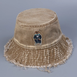 Close-up of embroidered bear and raw fringe edges on washed denim bucket hat