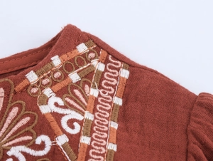Detailed close-up of intricate geometric floral embroidery on red cotton linen fabric