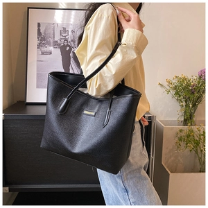 Close-up of black textured tote bag featuring a golden metallic logo plate on the side