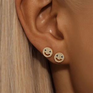 Close-up of golden smiley face earrings with sparkling white zircons and blue stone eyes