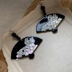 Detailed view of black fan-shaped earrings with white mother-of-pearl floral pattern