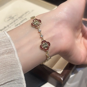 Gros plan d'un bracelet trèfle doré avec motifs rouges et zircons brillants au poignet