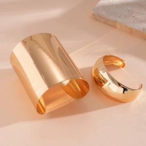 Detailansicht von zwei minimalistischen goldfarbenen, glatten, offenen Manschettenarmbändern