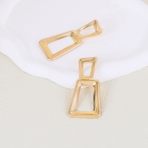 Exaggerated golden geometric earrings with double rectangular nested design on white tray