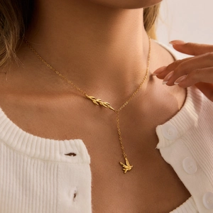 Detail of 18K gold-plated Y-necklace featuring frosted leaf accents and a dove bird charm