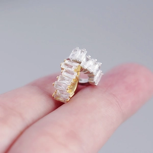 Detailed close-up of golden S925 silver earrings with rectangular zircon stones on a finger