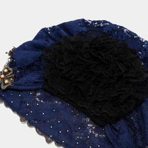 Détail du turban en dentelle bleu foncé avec fleur noire, feuilles d'or et perles