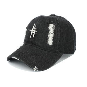 Detail of distressed black denim baseball cap with metal logo and ripped hole texture