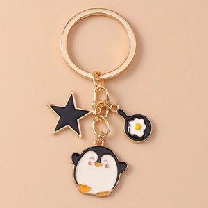 Detail of golden metal keychain with penguin, fried egg pan and black star charms