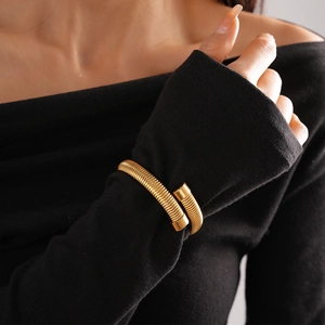 Detailed view of a gold metallic snake spring bracelet on a black sleeve
