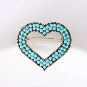 Detailed view of heart-shaped bronze brooch with turquoise beads on a white surface
