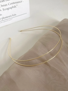 Detail shot of a minimalist double-layered gold metal headband on silk texture