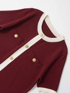 Close-up of burgundy knit cardigan featuring lion head gold buttons and white trim details