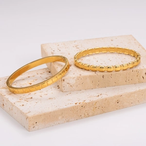 Minimalist gold stainless steel bracelets with geometric textures on beige marble base