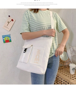 Detail of white canvas crossbody bag with NICE print and black plastic buckle strap