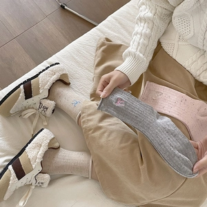 Detail of knit rib texture and embroidered bow on beige mid-calf socks with sneakers