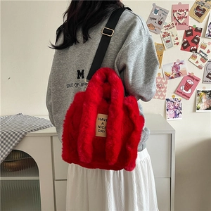 Fuzzy red plush tote bag with black adjustable strap worn by model in cozy home setting
