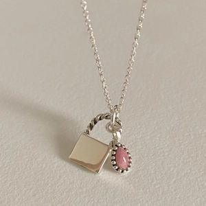 Close-up of a silver necklace featuring a square pendant and a pink teardrop gemstone