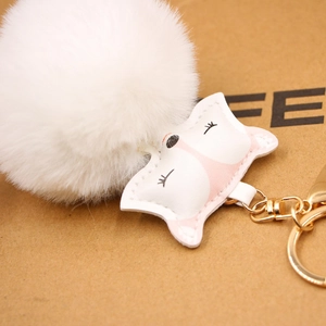 Detail of soft white faux fur pompom and pink leather fox charm on golden keychain