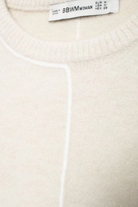 Detail view of the ribbed round neckline and brand label on a beige knit sweater