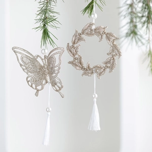 Glittery champagne gold butterfly and wreath ornaments with white tassels on pine branch