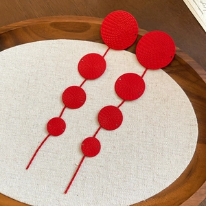 Detailed macro view of long red multi-disc earrings with spiral textures on a wooden tray