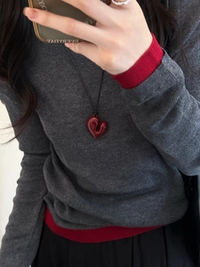 Dettaglio della collana con ciondolo a cuore rosso e cordino nero su maglia grigia