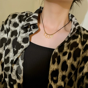 Minimalist golden LOVE pendant necklace with black cord shown on model's neck