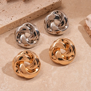 Metallic twisted knot stud earrings in gold and silver finish on stone background