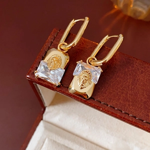 Macro shot of gold lion head earrings with sparkling rectangular zircons on jewelry box