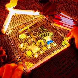 Close-up of a hand drawing cartoon patterns on a glowing acrylic LED message board