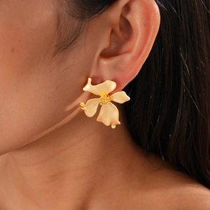 Detail von mattgoldenen Blumenohrringen mit matter Textur am Ohr eines Modells