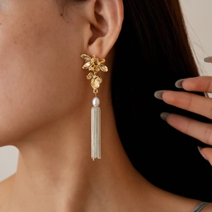 Gros plan de boucles d'oreilles fleur avec perles et pompons portées par un modèle