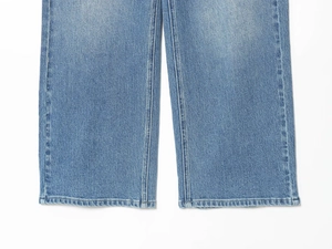 Detailed close-up showing the blue denim texture and premium hem stitching of wide-leg jeans