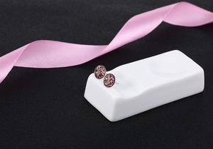 Close-up of glitter-filled round stud earrings in pinkish-purple on a ceramic stand