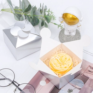 Silver laser paper gift box with petal fold closure and a yellow flower candle inside