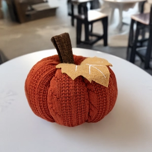 Detailansicht eines orangefarbenen Strickkürbisses mit gelben Filzblättern auf weißem Tisch