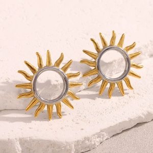 Detail of sunburst earrings in gold and silver tones on a textured white stone base