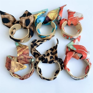 Detail showing six styles of matte gold silk scarf bracelets with vibrant artistic prints