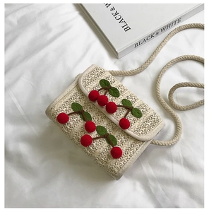 Close-up of woven straw square bag with red 3D cherries and braided rope strap
