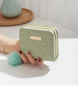 Detail of light green quilted faux leather wallet with double zippers and pompom