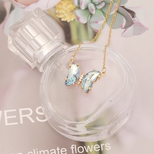Detail of butterfly pendant with light blue faceted crystal on a gold chain necklace