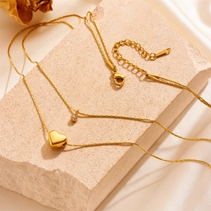 Double-layered gold heart necklace with zircon pendant on stone and silk background