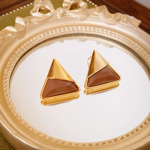 Macro detail of geometric gold and amber resin earrings on a vintage mirror tray
